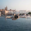 DJI Mini 4 Pro Drohne schwebt über dem Meer mit toskanischer Stadt im Hintergrund