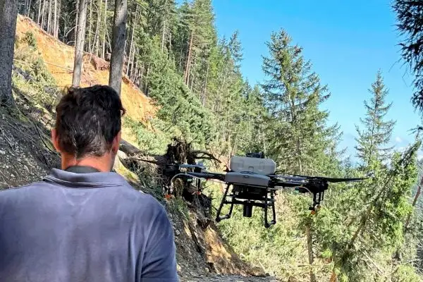 Agrardrohnen DJI Agras T10 fliegt über einen Murenabgang und bringt eine Saatgutmischung zur Neuanlage von Wiesensaatgut aus